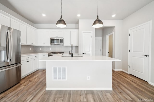 kitchen featuring sink, hanging light fixtures, stainless steel appliances, and an island with sink