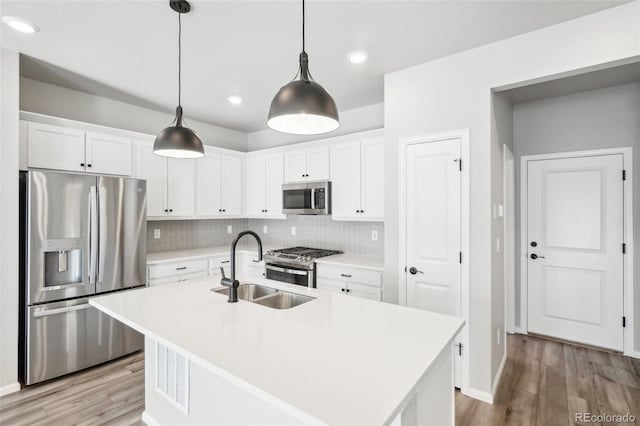 kitchen featuring decorative light fixtures, sink, a kitchen island with sink, appliances with stainless steel finishes, and white cabinets