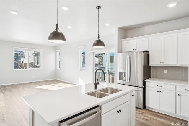 kitchen featuring stainless steel appliances, tasteful backsplash, a kitchen island with sink, pendant lighting, and sink