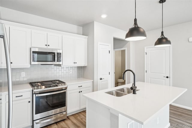 kitchen featuring white cabinetry, stainless steel appliances, a kitchen island with sink, hanging light fixtures, and sink