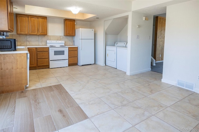 kitchen with washing machine and clothes dryer, brown cabinetry, visible vents, white appliances, and light countertops