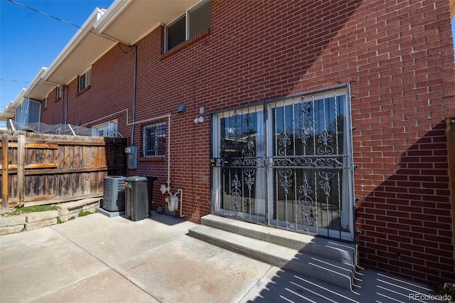 back of property with central air condition unit, fence, brick siding, a patio, and entry steps