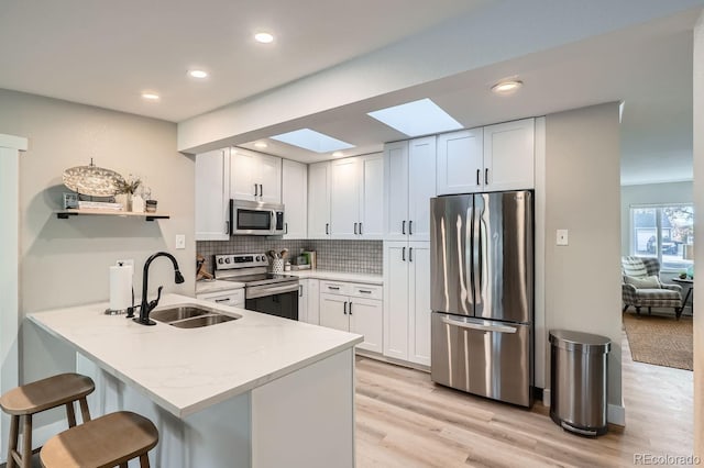 kitchen featuring a skylight, sink, white cabinets, and stainless steel appliances