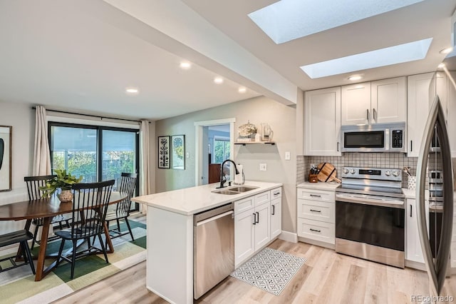 kitchen with stainless steel appliances, white cabinetry, a skylight, and sink