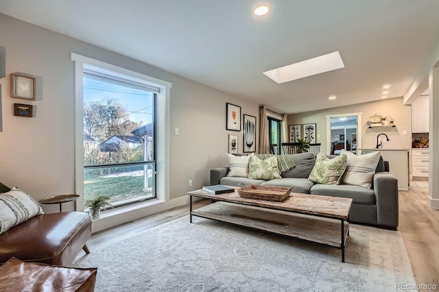 living room featuring a skylight, a wealth of natural light, light hardwood / wood-style flooring, and sink