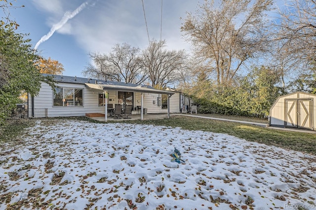 snow covered back of property featuring a storage shed, a yard, and a patio