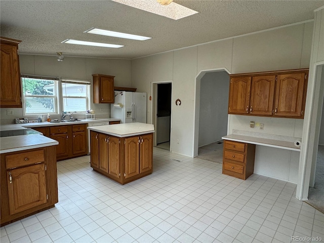 kitchen featuring white fridge with ice dispenser, a textured ceiling, a center island, sink, and lofted ceiling with skylight