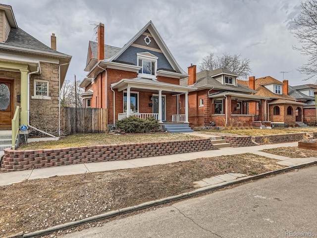 view of front facade featuring a porch, fence, and brick siding