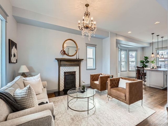 living room with wood-type flooring, recessed lighting, baseboards, a tiled fireplace, and an inviting chandelier