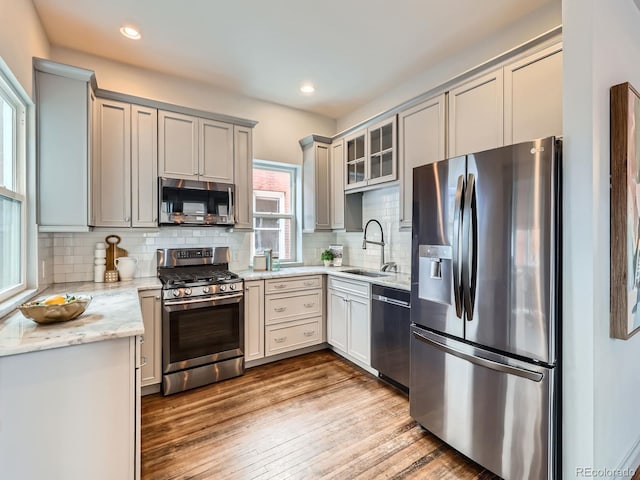 kitchen with light stone counters, light wood-style flooring, stainless steel appliances, a sink, and backsplash