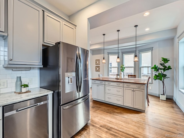 kitchen with stainless steel appliances, butcher block countertops, light wood-type flooring, and backsplash