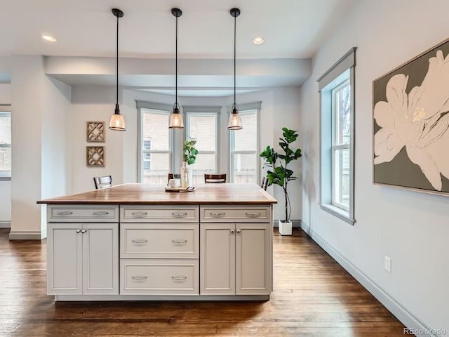 kitchen with baseboards, dark wood finished floors, a kitchen island, wood counters, and decorative light fixtures