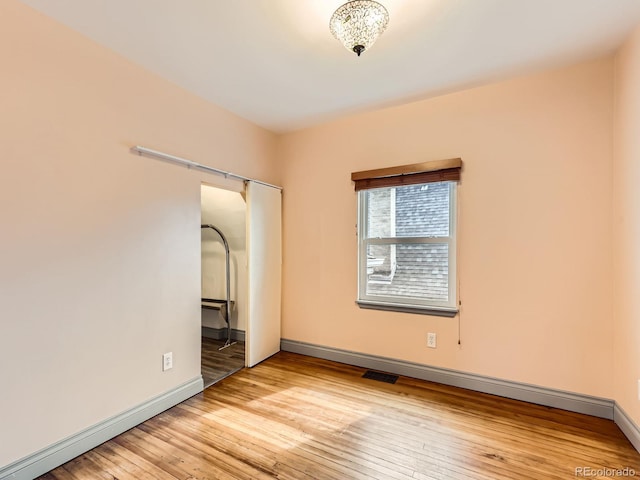 spare room with wood-type flooring, visible vents, and baseboards