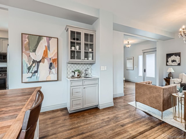 bar featuring baseboards, backsplash, stainless steel microwave, gas stove, and dark wood finished floors