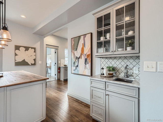 kitchen with butcher block countertops, glass insert cabinets, dark wood-type flooring, a sink, and backsplash