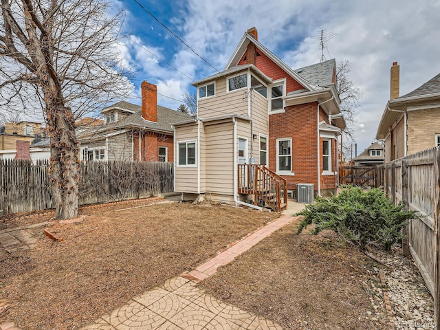 rear view of house with brick siding, a fenced backyard, and central air condition unit