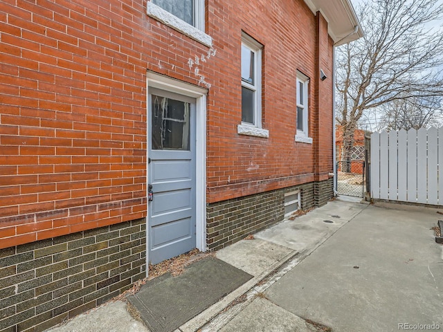 doorway to property with brick siding, fence, and a gate