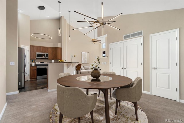 dining area featuring light carpet, a towering ceiling, and ceiling fan with notable chandelier