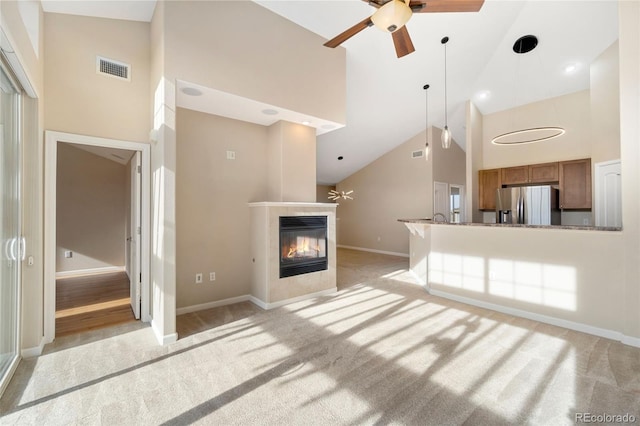 unfurnished living room with ceiling fan, light colored carpet, a fireplace, and high vaulted ceiling