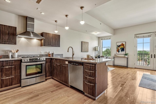 kitchen with dark brown cabinets, appliances with stainless steel finishes, wall chimney exhaust hood, and a sink