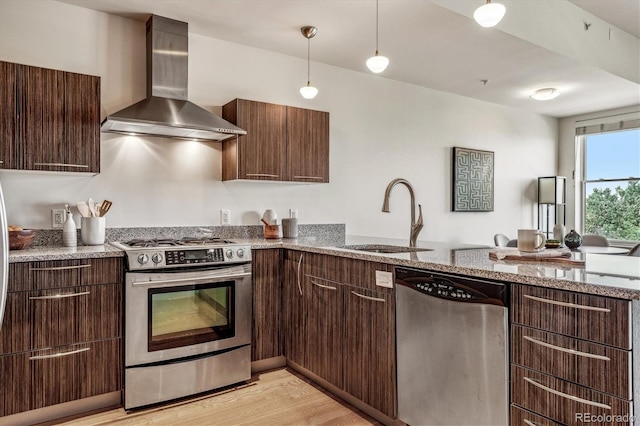 kitchen with dark brown cabinets, appliances with stainless steel finishes, wall chimney range hood, and a sink