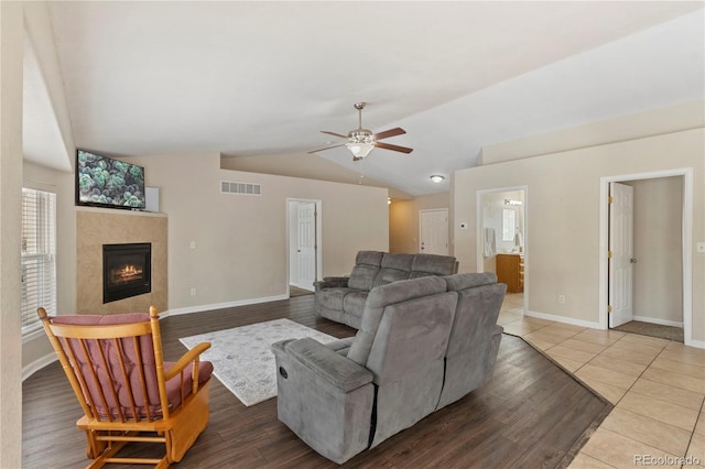 living room featuring a tiled fireplace, vaulted ceiling, wood-type flooring, and ceiling fan