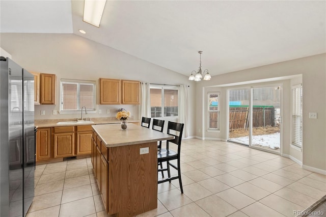 kitchen featuring a kitchen island, stainless steel refrigerator, sink, hanging light fixtures, and light tile patterned floors