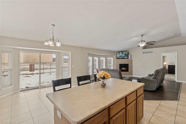 kitchen featuring hanging light fixtures, a kitchen island, light tile patterned flooring, ceiling fan with notable chandelier, and vaulted ceiling