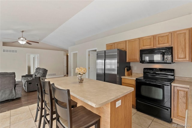 kitchen with light tile patterned flooring, a kitchen island, a breakfast bar area, and black appliances