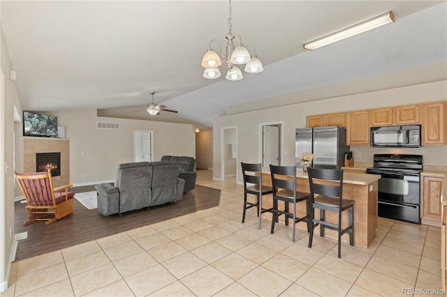 kitchen with lofted ceiling, light tile patterned floors, black appliances, a kitchen island, and decorative light fixtures