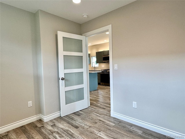 spare room with recessed lighting, wood finished floors, baseboards, and a sink