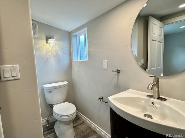 half bath featuring vanity, toilet, wood finished floors, and baseboards