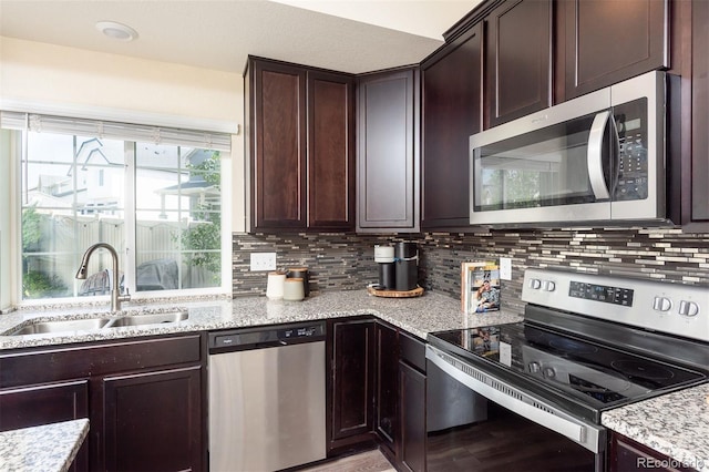 kitchen featuring sink, appliances with stainless steel finishes, backsplash, light stone counters, and dark brown cabinetry