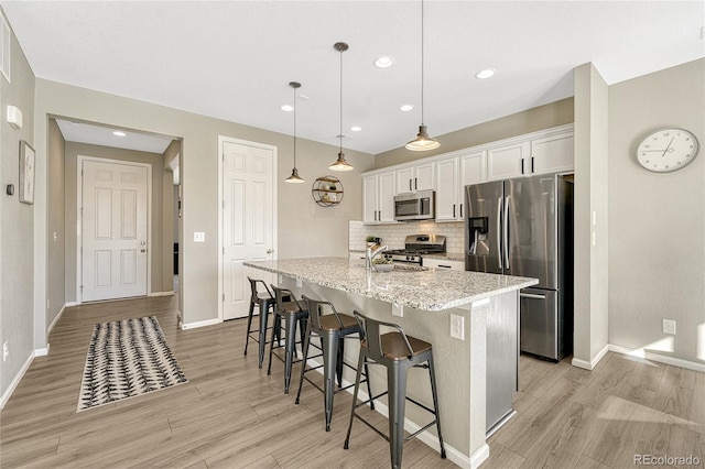 kitchen featuring white cabinetry, hanging light fixtures, a kitchen island with sink, stainless steel appliances, and light stone counters