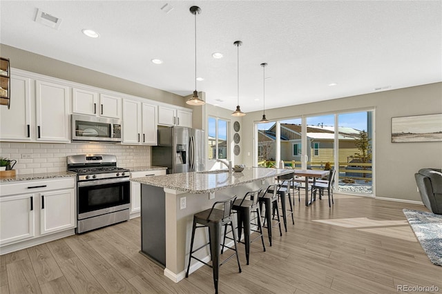 kitchen featuring appliances with stainless steel finishes, decorative light fixtures, white cabinetry, a kitchen breakfast bar, and a kitchen island with sink