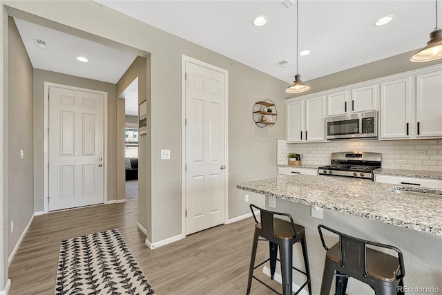 kitchen with hanging light fixtures, stainless steel appliances, tasteful backsplash, light stone countertops, and white cabinets