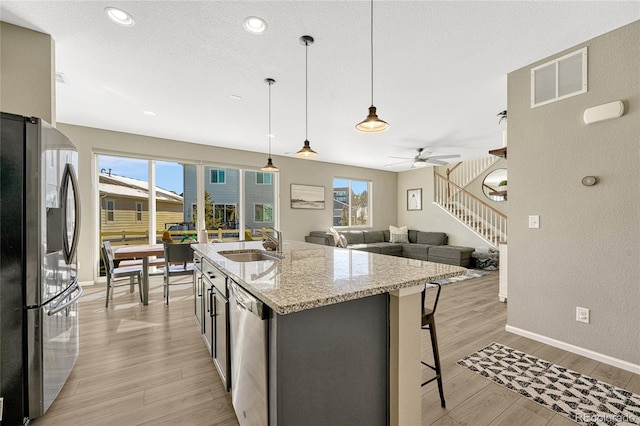 kitchen featuring appliances with stainless steel finishes, pendant lighting, sink, light stone counters, and a center island with sink