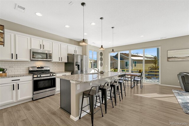 1886 Makley Loop, Castle Rock, CO 80104 - kitchen with appliances with stainless steel finishes, light wood-type flooring, tasteful backsplash, an island with sink, and white cabinets