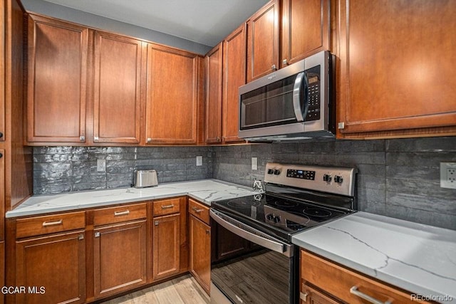 kitchen featuring light stone counters, stainless steel appliances, decorative backsplash, and light wood-style flooring