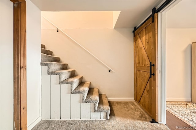 stairs with a barn door, carpet, and baseboards