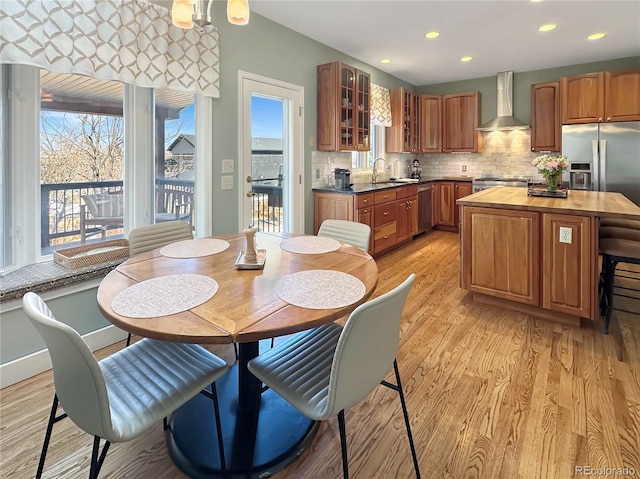 kitchen with light wood-type flooring, appliances with stainless steel finishes, wall chimney range hood, decorative backsplash, and wooden counters