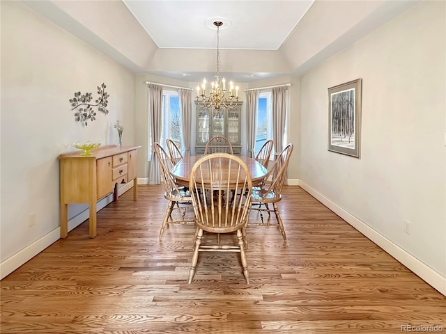 dining space with baseboards, a raised ceiling, a chandelier, and light wood finished floors