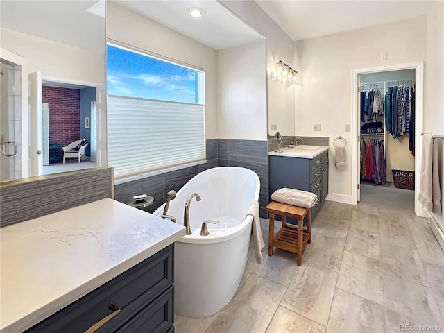 full bathroom featuring a soaking tub, vanity, and a walk in closet