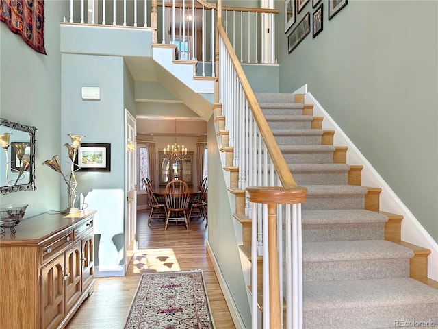 staircase with a notable chandelier, wood finished floors, baseboards, and a towering ceiling