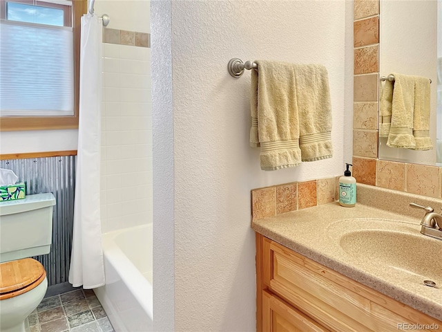 full bathroom featuring toilet, stone finish floor, shower / bath combination with curtain, vanity, and a textured wall