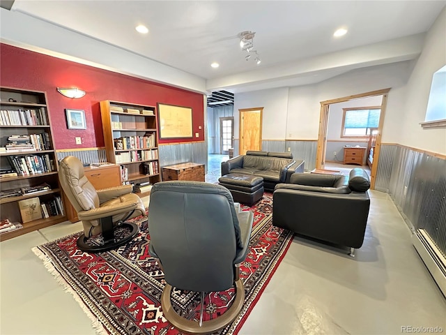 living area with a wealth of natural light, a wainscoted wall, concrete floors, and a baseboard heating unit