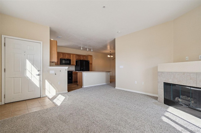 unfurnished living room with light tile patterned floors, rail lighting, light carpet, a tile fireplace, and baseboards