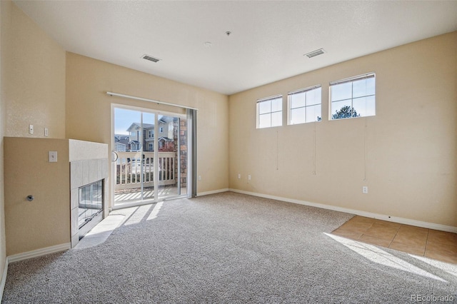 empty room with light carpet, baseboards, a premium fireplace, and visible vents