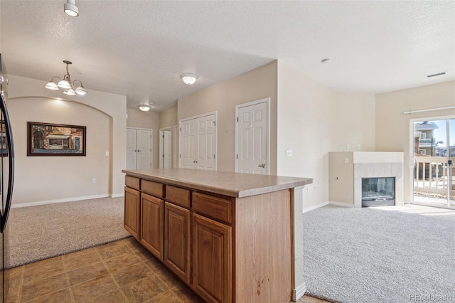 kitchen with open floor plan, decorative light fixtures, light countertops, carpet flooring, and a fireplace