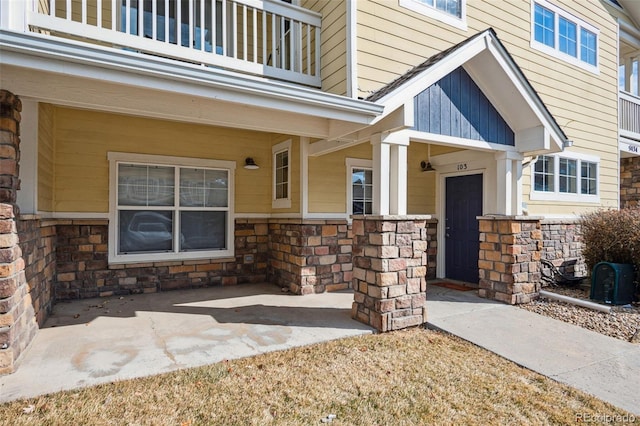 doorway to property with stone siding, a patio area, and a balcony